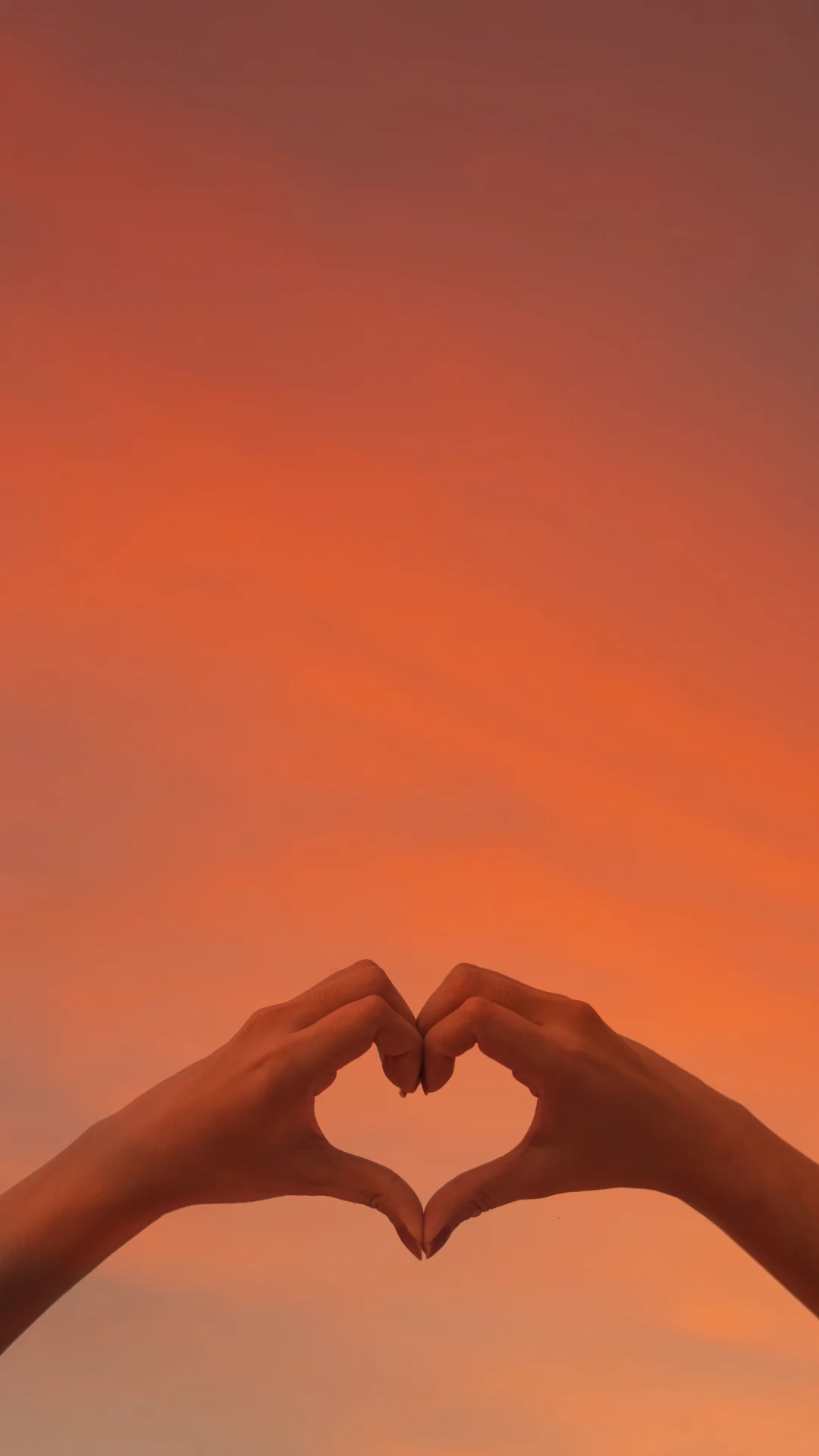 Two hands forming a heart against an evening sky